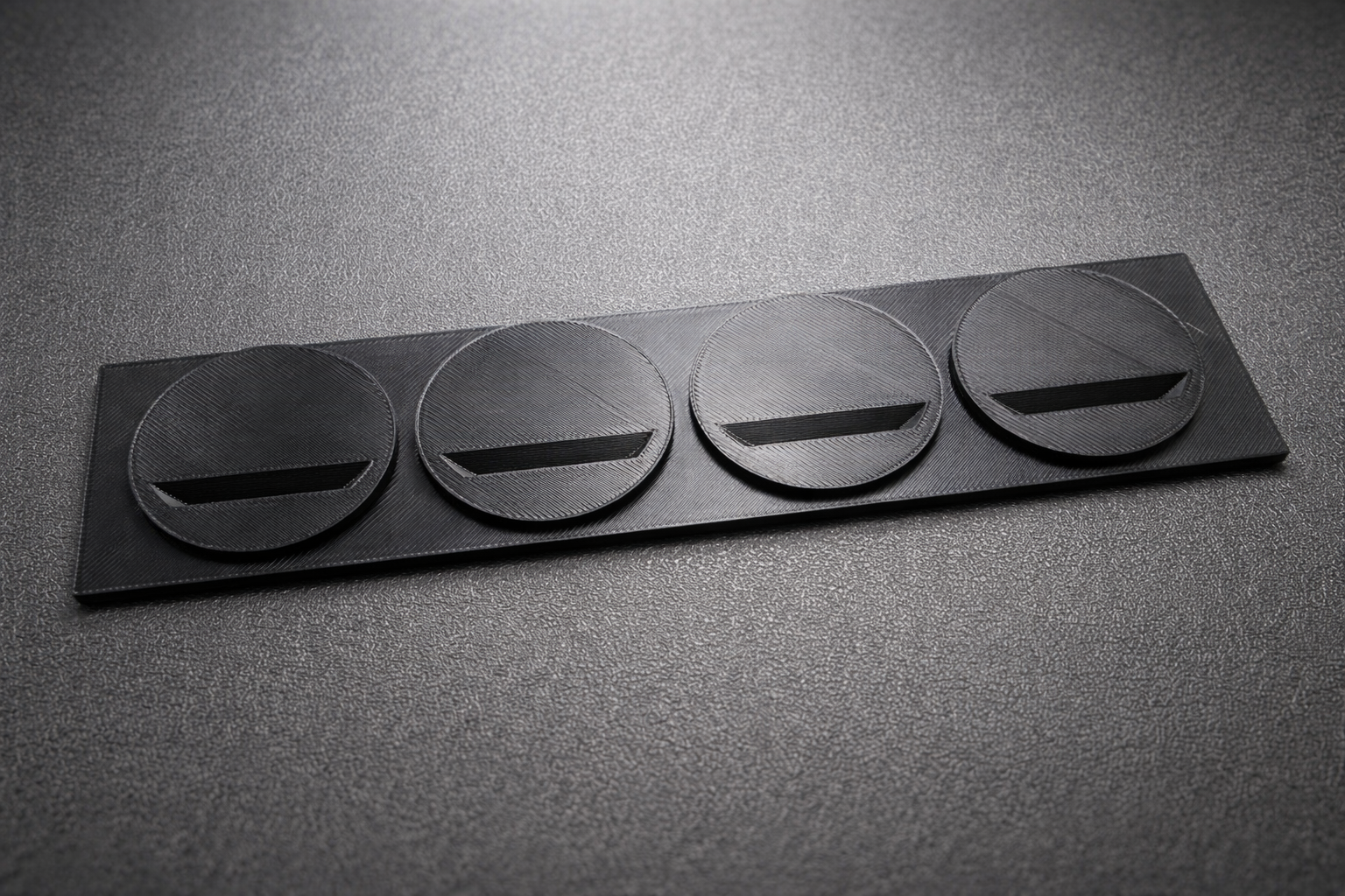 Black metallic plate with circular cutouts on a gray surface